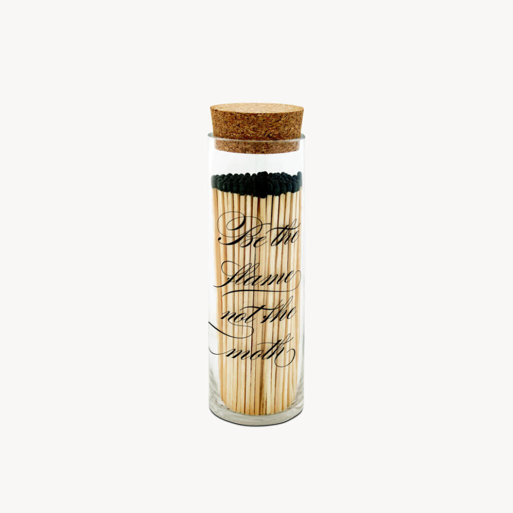 Our apothecary fireplace match bottles are a sophisticated and updated option for storing your matches, featuring a silk-screened design and cork lid. The Calligraphy design is silk-screened with the phrase "Be the flame not the moth". The bottle features our exclusive strike-on-bottle design and has a striker strip on the back of the bottle for lighting all 120 matches in style.  Hand-made in the USA   • 120 - 8" Matchsticks • Strike-on-bottle flint • 10 1/2" high x 3" wide